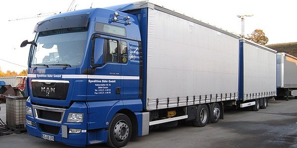 Blau-weißer MAN-Hängerzug mit zwei Planenaufbauten auf dem Hof; an der Fahrertür der Schriftzug Spedition Bähr GmbH mit Anschrift und Rufnummer.